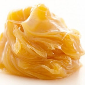 May include: A close-up of a golden yellow, thick, and viscous substance. The substance is smooth and shiny, with a slightly textured surface.