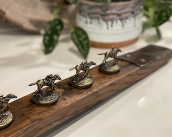 Può includere: Un tagliere di legno con quattro figurine di cavallo e fantino in metallo attaccate. Il tagliere è marrone scuro con venature del legno naturali. Le figurine sono dorate e sono disposte in fila.