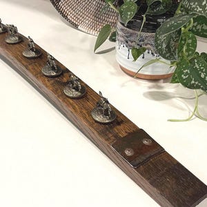 May include: A wooden barrel stave with a metal plate and multiple small metal figurines attached to it. The figurines are of people in various poses.