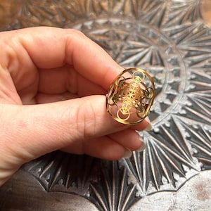 May include: Gold-toned ring featuring a geometric design resembling a flower of life. The ring is made of metal and has a delicate, intricate pattern.