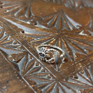 May include: A silver ring with a scorpion design. The scorpion's tail is curled up and its stinger is visible. The ring is on a wooden surface.