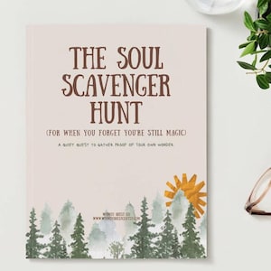 Puede incluir: Un diario titulado "THE SOUL SCAVENGER HUNT" con el texto "(FOR WHEN YOU FORGET YOU'RE STILL MAGIC)". La portada presenta una ilustración de un bosque y un sol. El diario está sobre una superficie blanca.