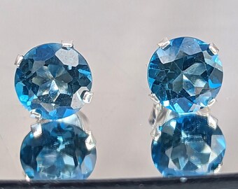 May include: A pair of silver stud earrings with round, faceted, blue topaz gemstones.