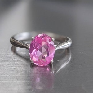 May include: A silver ring with a large oval pink gemstone.