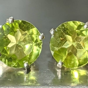 May include: A pair of silver earrings with round green peridot gemstones.