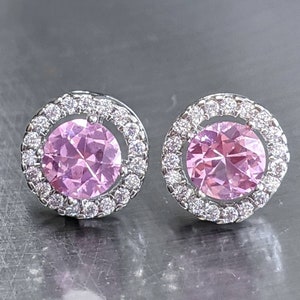 May include: A pair of silver stud earrings with a pink gemstone surrounded by a halo of smaller clear gemstones.