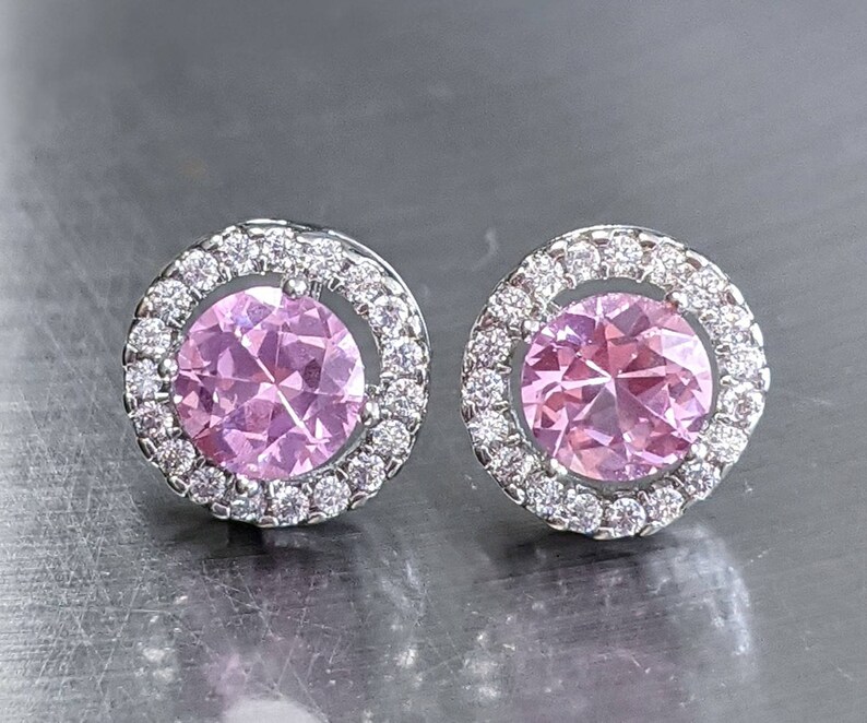 May include: A pair of silver stud earrings with a pink gemstone surrounded by a halo of smaller clear gemstones.