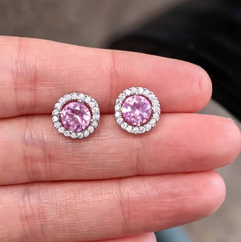 May include: A pair of silver stud earrings with a pink gemstone surrounded by a halo of smaller clear gemstones.