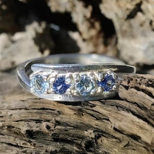 May include: A silver band ring with three blue gemstones set in a twisted band.