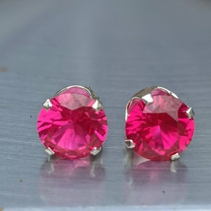 May include: A pair of silver stud earrings with bright pink round gemstones.