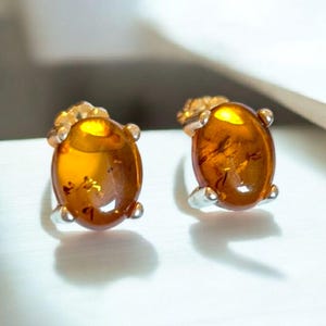 May include: A pair of oval amber earrings with silver settings. The earrings are set in a simple, classic style.