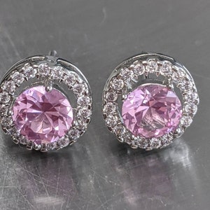 May include: A pair of silver stud earrings with a pink gemstone surrounded by a halo of smaller clear gemstones.