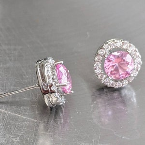May include: A pair of silver earrings with a pink gemstone surrounded by a halo of smaller clear gemstones.