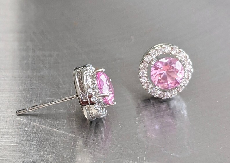 May include: A pair of silver earrings with a pink gemstone surrounded by a halo of smaller clear gemstones.