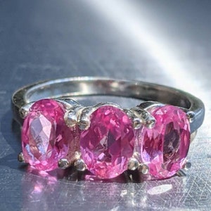 May include: A silver ring with three oval-shaped pink gemstones set in a row.