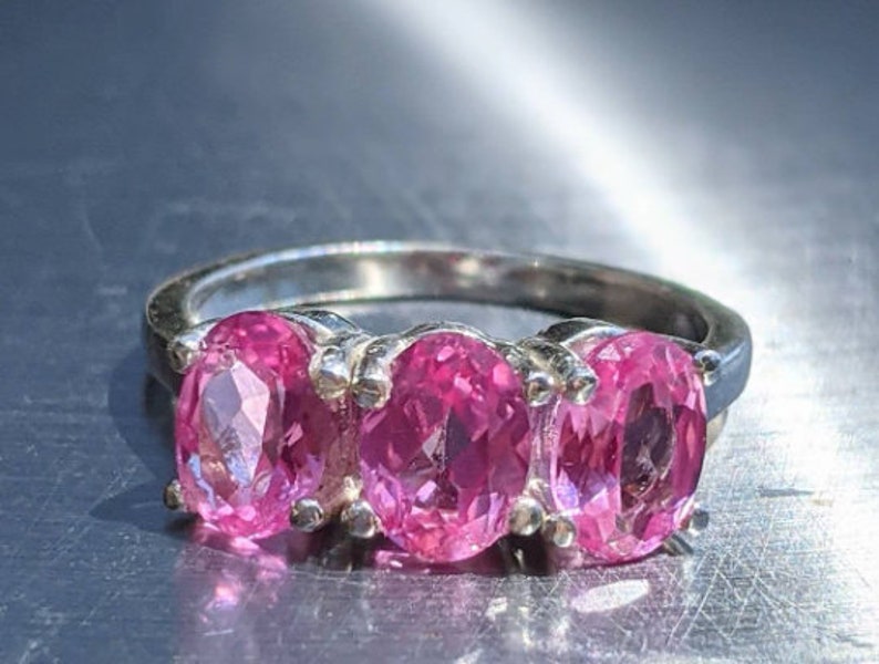 May include: A silver ring with three oval-shaped pink gemstones set in a row.