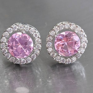 May include: A pair of silver earrings with a pink gemstone surrounded by a halo of smaller clear gemstones.