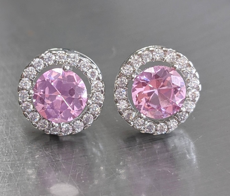May include: A pair of silver earrings with a pink gemstone surrounded by a halo of smaller clear gemstones.
