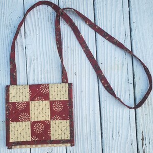 May include: A small red and cream quilted bag with a long red strap. The bag has a patchwork design with different patterns of stars and dots.
