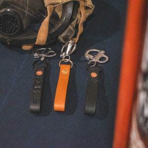 May include: Three leather keychains with metal clasps. The keychains are black, brown, and tan.