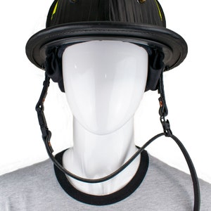 以下が含まれることがあります： 黄色いストライプとあご紐が付いた黒い革のヘルメット。ヘルメットは白いマネキンの頭に置かれています。