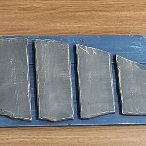Puede incluir: Un letrero de madera con fondo azul y una forma de pez gris hecha de piezas individuales de madera. El letrero tiene el texto "Love of Beach Home Designs" en un c&iacute;rculo.