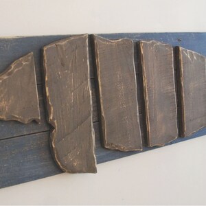 Puede incluir: Una pieza de arte de pared de madera con forma de concha, hecha de tablones de madera recuperados. La concha est&aacute; pintada de marr&oacute;n y montada sobre un fondo de madera pintado de azul. La pieza est&aacute; firmada con "Love of Beach Home Designs".