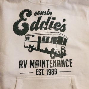 May include: White hoodie with a black graphic print of a vintage RV with the text "cousin Eddie's RV Maintenance Est. 1989".