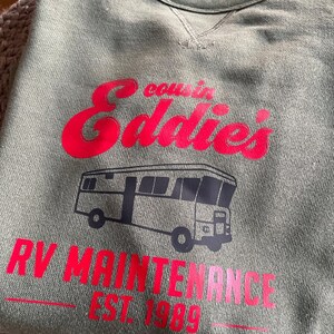 May include: Green sweatshirt with a red graphic that says "cousin Eddie's RV Maintenance Est. 1989". The graphic also includes a black and white illustration of a recreational vehicle.