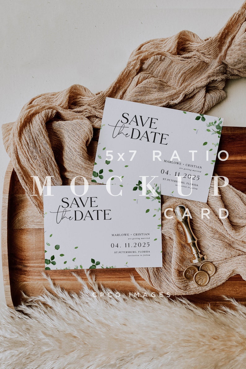 May include: A mockup of a save the date card with a 5x7 ratio. The card is white with a light blue background and features a green leafy design. The text on the card reads "Save the Date" and includes the names "Marlowe & Cristian" and the date "04.11.2025". The card is sitting on a wooden tray with a piece of beige fabric and a gold wax seal.