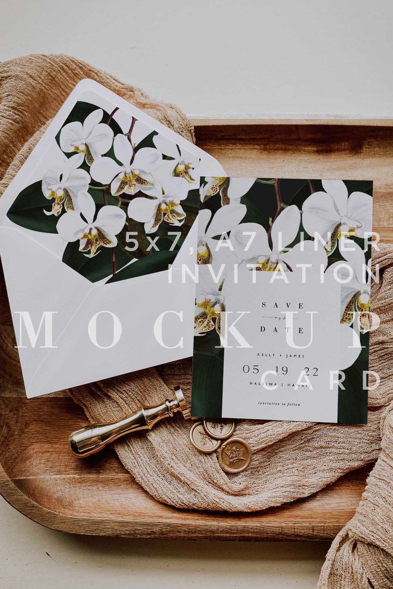 Op de afbeelding: Een witte envelop met een bloemenontwerp aan de voorkant, een witte A7-liner uitnodiging met een bloemenontwerp, een gouden waszegel en een houten dienblad met een bruine stof erop. De uitnodiging zegt "Save the Date" met de datum "05 19 22" en de locatie "Halawa, Hawaii".