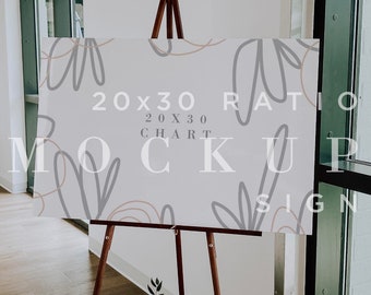 May include: A wooden easel with a white sign displaying a 20x30 ratio chart mockup. The sign has a light gray background with abstract lines in pink and gray. The text on the sign reads "20x30 Ratio Chart Mockup Sign".
