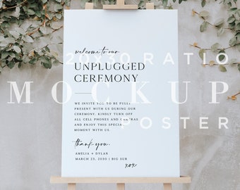 May include: A white sign with a wooden easel, featuring the text "Welcome to our Unplugged Ceremony" and a message asking guests to turn off their phones and cameras. The sign also includes the names Amelia and Dylan, the date March 23, 2030, and the location Big Sur.
