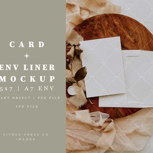 May include: A mockup of a white card and envelope liner on a wooden surface with a beige fabric background. The card and envelope liner are blank and ready for customization. The text "CARD + ENV LINER MOCKUP 5x7 | A7 ENV SMART OBJECT | PSD FILE JPG FILE" is displayed on the left side of the image.