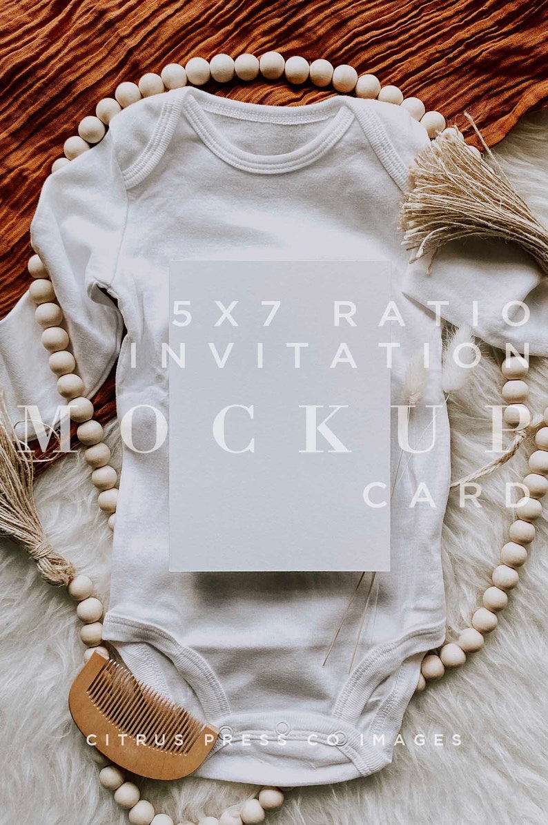 Pu&ograve; includere: Un body bianco per neonato con un mockup di carta da invito vuoto in formato 5x7 in cima. Il body &egrave; circondato da una ghirlanda di perline di legno e una superficie bianca e soffice. Il testo "5x7 Ratio Invitation Mockup Card" &egrave; stampato sulla carta.