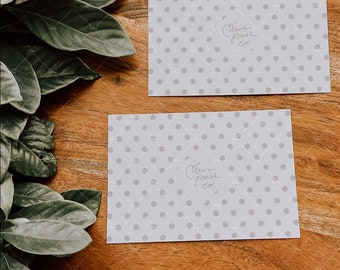 May include: Two white cards with a light gray polka dot pattern and the text "Citrus Press Co." written in cursive. The cards are on a wooden surface with green leaves.