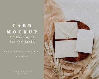 May include: A mockup of two white envelopes and a white card on a wooden tray. The envelopes are A7 size and the card is 5x7 inches. The tray is surrounded by a beige fabric and white dried flowers.