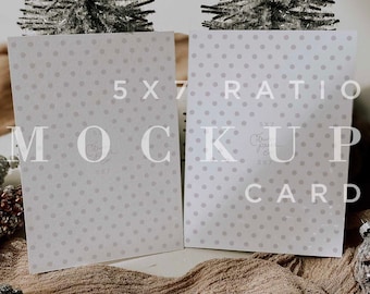 May include: Two white cards with a gray polka dot pattern. The cards are blank and have the text "5x7 Ratio Mockup Card" printed on them. The cards are sitting on a brown fabric surface with two small silver trees on either side.