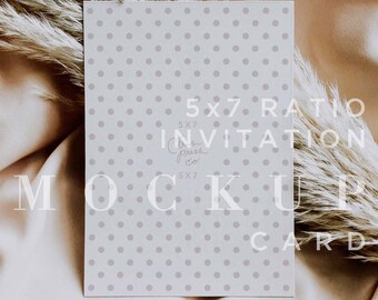 May include: A white card with a light gray polka dot pattern. The card has the text "5x7 Ratio Invitation" and "Mockup Card" printed on it. The card is lying on a light brown fabric surface.