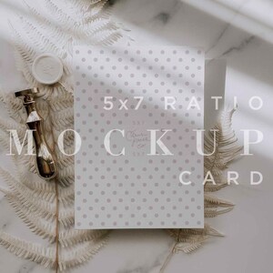 May include: A white card with a gray polka dot pattern. The card is laying flat on a white marble surface with a sprig of dried ferns on either side. The card has the text "5x7 Ratio Mock Up Card" printed on it.