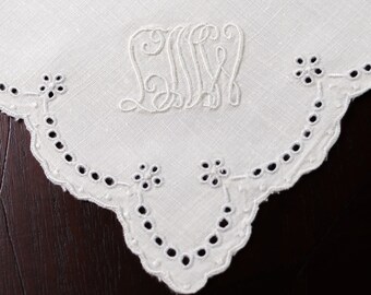 May include: White linen napkin with a scalloped edge and embroidered initials. The napkin has a delicate lace pattern around the edge.