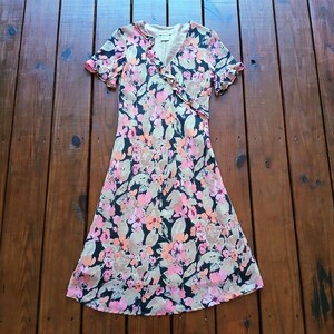 May include: A black and beige floral print dress with a V-neckline and short sleeves. The dress has a wrap style and a flowing skirt.