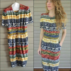 May include: A vintage midi dress with a colorful striped pattern featuring a variety of floral and geometric designs. The dress has a button-up front, short sleeves, and a fitted silhouette.
