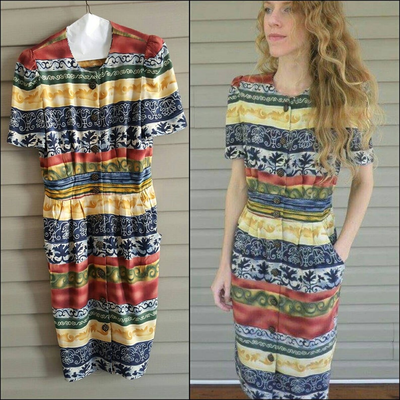 May include: A vintage midi dress with a colorful striped pattern featuring a variety of floral and geometric designs. The dress has a button-up front, short sleeves, and a fitted silhouette.