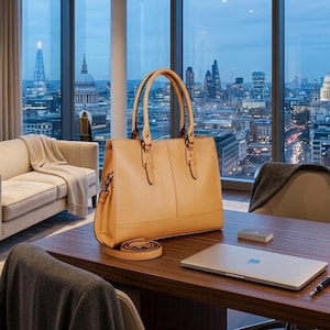 May include: A tan leather tote bag with two top handles and a detachable shoulder strap. The bag features a structured rectangular shape with vertical seam detailing on the front panel and metallic hardware connecting the handles to the body.