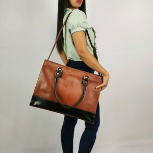 May include: A brown leather tote bag with a black base and gold hardware. The bag has two top handles and a long shoulder strap.