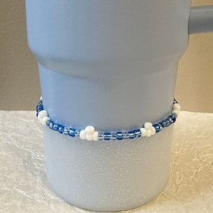 May include: A light blue mug with a white and blue beaded trim. The bottom half of the mug is covered in white glitter.