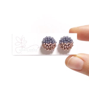 May include: A pair of small, round earrings with a gradient of gray and rose gold beads. The earrings are displayed on a white card with the text "Federica Daniele Creative Accessories".
