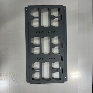 May include: Black metal wall mount with a grid of rectangular cutouts. The mount has a total of 12 cutouts, arranged in three rows of four.