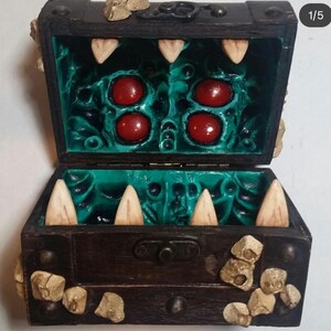 Puede incluir: Un cofre del tesoro de madera con exterior marr&oacute;n oscuro e interior turquesa. El interior presenta grandes formas redondas rojas y dientes blancos y puntiagudos. El cofre est&aacute; decorado con peque&ntilde;as piedras de color beige.